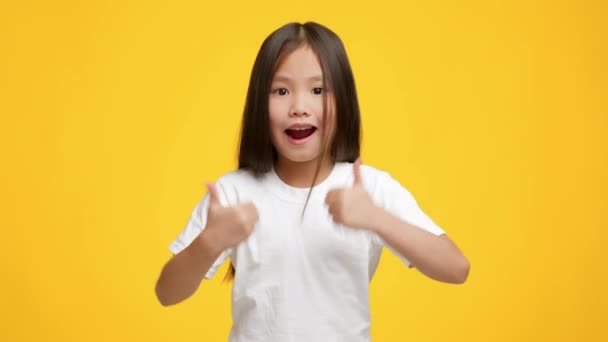 Kleines asiatisches Mädchen gestikuliert mit dem Daumen nach oben und posiert vor gelbem Hintergrund — Stockvideo