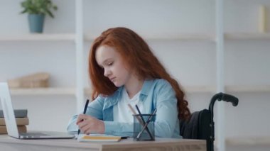 Tekerlekli sandalyeli yorgun küçük kız evde ders çalışıyor, canı sıkkın, baş ağrısı çekiyor, yakınlaştır.