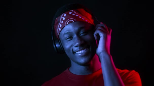 Fekete fickó visel fejhallgató hallgat zenét sötét stúdióban — Stock videók