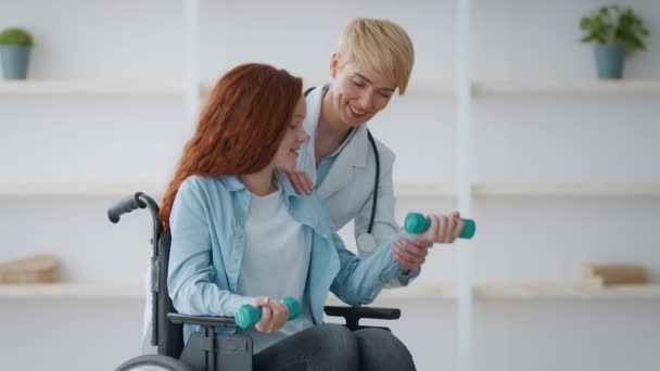 Reabilitação após acidente. Média idade médico mostrando exercício com halteres para menina com deficiência — Vídeo de Stock