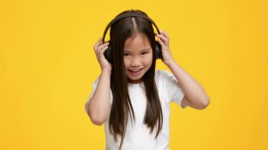 Müzik dinleyen küçük Asyalı kız kulaklık takıyor, sarı arka plan