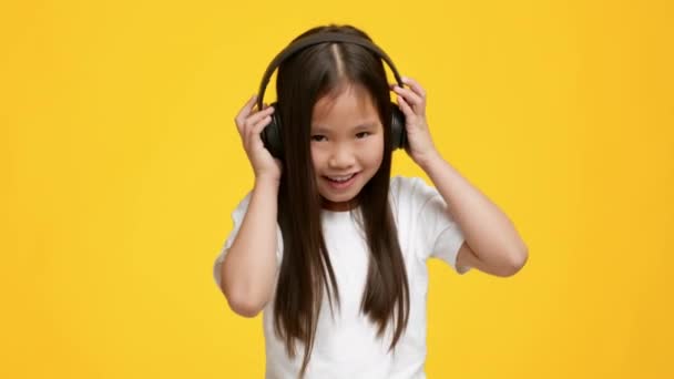 Menina asiática escutando música usando fones de ouvido, fundo amarelo — Vídeo de Stock