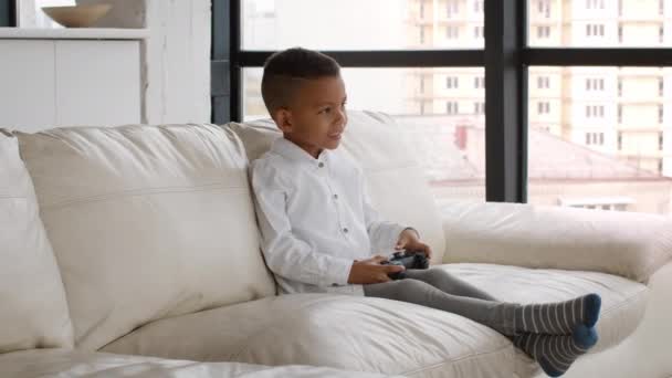 Молодой Геймер. Маленький чернокожий мальчик держит в руках джойстик, играя дома в видеоигры — стоковое видео