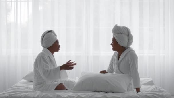 Duas irmãs afro-americanas alegres vestindo roupões de banho conversando e rindo em casa — Vídeo de Stock