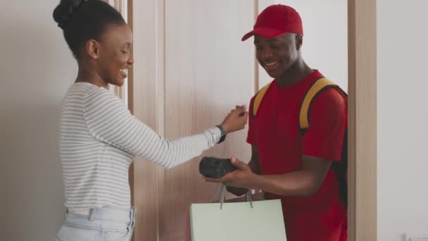 Νεαρή Αφρικάνα Αμερικανίδα κυρία που πληρώνει για παραγγελία από μπουτίκ μόδας με smartwatch και να πάρει τσάντες από courier — Αρχείο Βίντεο