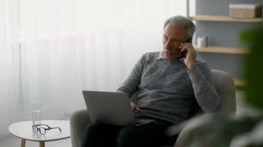 Emeklilik üzerine serbest çalışma. Evde cep telefonu ve laptop kullanan kıdemli bir adam.