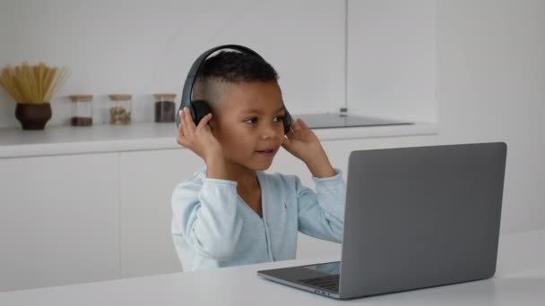 Schattig klein zwart jongen dragen draadloze hoofdtelefoon luisteren muziek online op de computer — Stockvideo