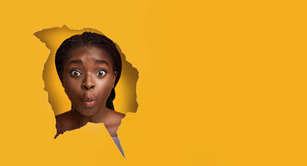 Удивлённая чёрная женщина смотрит через бумажную дыру.