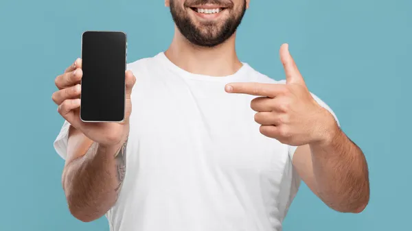 Веселий дорослий європеєць, який показує пальцем смартфон з чистим екраном і рекомендує ґаджет. — стокове фото