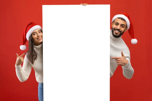 Noel Baba şapkalı genç adam ve kadın Noel Baba 'nın boş reklam panosuyla poz veriyor. — Stok fotoğraf