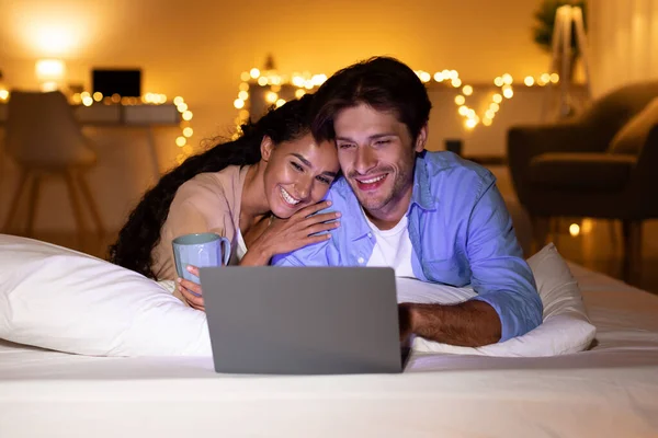 Cônjuges assistindo filme no laptop deitado na cama em casa — Fotografia de Stock