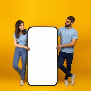 Güzel mobil uygulama. Milenyum Arap eşleri dev akıllı telefonun yanında duruyor ve uygulama veya web sitesini tanıtıyorlar.