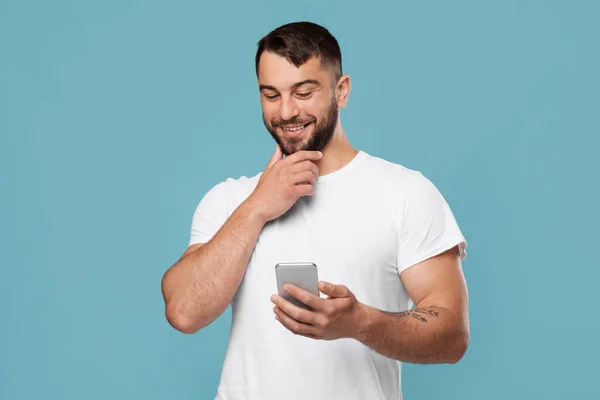 Happy pensive aantrekkelijke volwassen europees guy blogger typen op smartphone geïsoleerd op blauwe achtergrond — Stockfoto