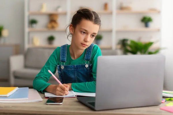 Κορίτσι κάθεται στο γραφείο, γράφοντας στο βιβλίο χρησιμοποιώντας το PC — Φωτογραφία Αρχείου