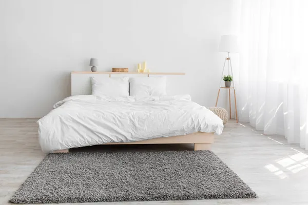 Cama de casal, tapete cinza macio e lâmpada no chão, móveis com acessórios, janela com cortinas — Fotografia de Stock