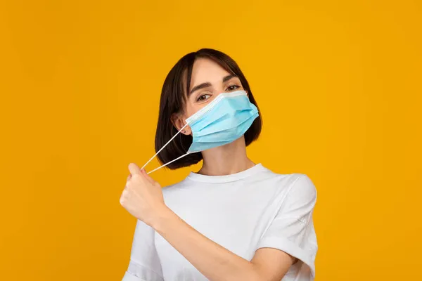 Конец эпидемии. Девушка снимает защитную маску, стоя изолированно на жёлтом фоне студии — стоковое фото
