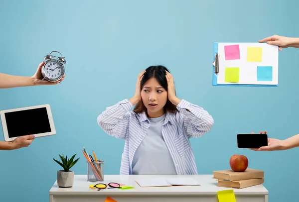 Стрессовая работа. Азиатка устала от работы, сидя за столом на синем фоне студии и трогая голову — стоковое фото
