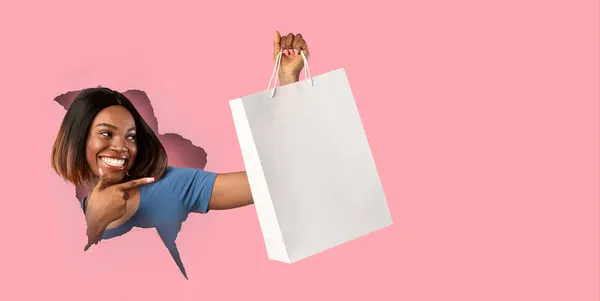 Mujer negra sosteniendo apuntando a la bolsa de comprador a través de un agujero de papel —  Fotos de Stock