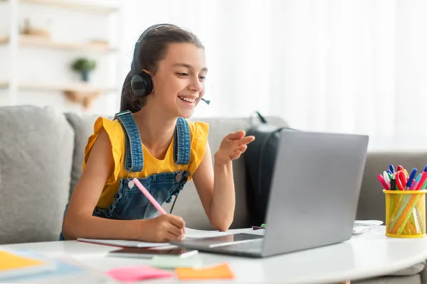 Menina sorridente no fone de ouvido usando laptop, falando durante a videocall — Fotografia de Stock