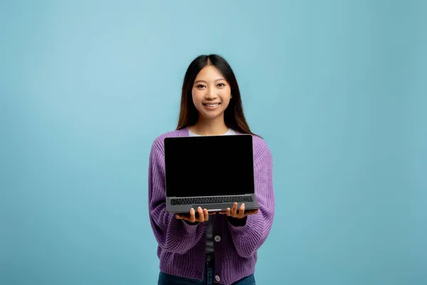 Χαμογελαστή ασιάτισσα κυρία δείχνει φορητό υπολογιστή με λευκή οθόνη για διαφήμιση, ενώ στέκεται πάνω από το μπλε φόντο, mockup — Φωτογραφία Αρχείου