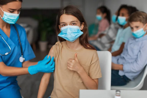 Chica vacunada usando máscara facial y gestos pulgares hacia arriba en interiores —  Fotos de Stock