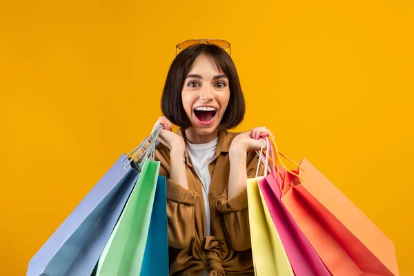 Wow concepto de ventas estacionales. Mujer muy alegre sosteniendo gran cantidad de bolsas de compras brillantes, posando sobre fondo amarillo —  Fotos de Stock