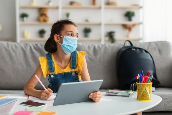 Sad girl in medical mask studying at home with tablet — Stock Photo, Image
