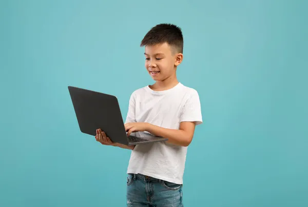 Portret małego azjatyckiego chłopca korzystającego z laptopa stojącego nad niebieskim tłem — Zdjęcie stockowe