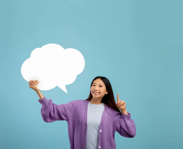 Bonita senhora asiática segurando bolha de fala em branco e fazendo gesto IDEA, de pé sobre fundo azul, mockup, espaço livre — Fotografia de Stock