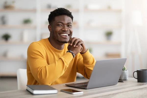 Black man freelancer sitting at workdesk at home, using laptop