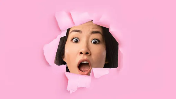 Εντυπωσιακό συγκλονιστικό συναίσθημα νεαρή ιαπωνική γυναίκα με ανοιχτό το στόμα ματιά σε τρύπα σε ροζ χαρτί — Φωτογραφία Αρχείου
