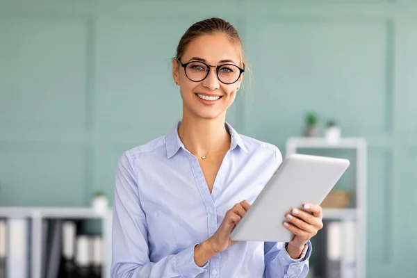 Happy business dame met behulp van tablet pc op haar werkplek in modern kantoor interieur en glimlachen op de camera — Stockfoto