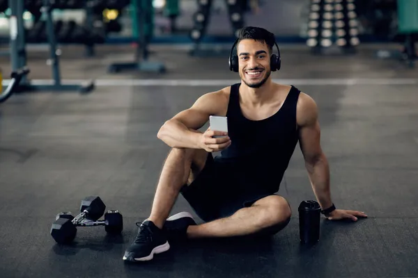 Bonito atleta árabe relaxante com smartphone após o treinamento em ginásio — Fotografia de Stock