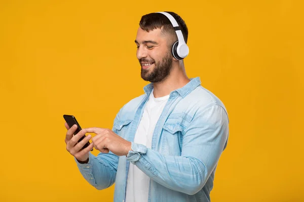 Feliz adulto europeu cara em fones de ouvido gostando de música favorita, digitando no smartphone — Fotografia de Stock