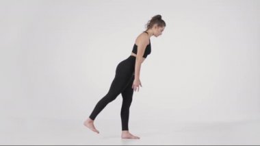 Temel yoga pozları. Bir bacağının üzerinde duran, öne doğru eğilen ve bacağını kaldıran genç bir kadının yan görünüm portresi.
