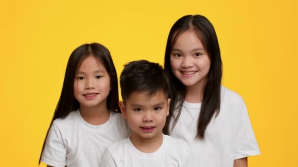 Dos hermanas japonesas felices y su hermanito posando, fondo amarillo — Vídeos de Stock