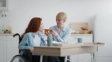 Sevgi dolu bir anne kızını engellilerle besliyor. Sıcak taze pizzayla. Evde tekerlekli sandalyede oturan kızıl saçlı bir kız.