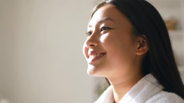 Close up retrato de jovem senhora coreana pobstive desfrutando de luz solar quente em casa, sorrindo à parte no espaço vazio — Vídeo de Stock