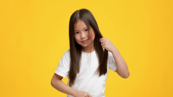 Κινέζικο κοριτσάκι Combing μακριά καστανή μαλλιά πάνω από κίτρινο φόντο — Αρχείο Βίντεο