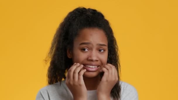 Налякана чорна дівчина-підліток кусає нігті пальцями в страху, жовтий фон — стокове відео