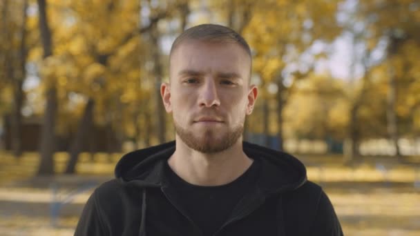 Közelkép portré fiatal békés szakállas férfi néz kamera, pózol fényes arany őszi parkban — Stock videók