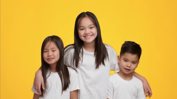 Szczęśliwy Azji dziewczyna przytulanie młodszy brat i siostra, żółty tło — Wideo stockowe