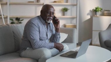 Serbest çalışmak ve emeklilik. Kıdemli Afro-Amerikan adam müşterilerine danışmanlık yapıyor cep telefonuyla konuşuyor ve dizüstü bilgisayarla çalışıyor.