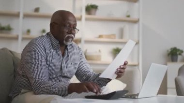 Emeklilik finansal planlama kavramı. Kıdemli Afro-Amerikan adam banka hesaplarını yönetiyor, bütçe vergisini hesaplıyor.