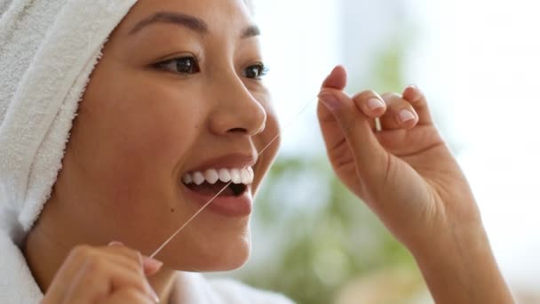 Fogászati higiénia. Közelkép egy fiatal ázsiai nőről, aki fogselyemmel mossa a fogát, törődik a mosollyal — Stock videók