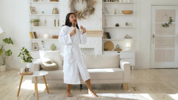 Jeune femme asiatique positive portant salle de bain ayant du plaisir, femme utilisant une brosse à cheveux comme micro, danse à la maison, ralenti — Video