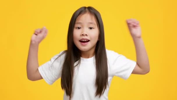 Feliz preescolar japonesa chica sacudiendo puños celebrando el éxito, fondo amarillo — Vídeos de Stock