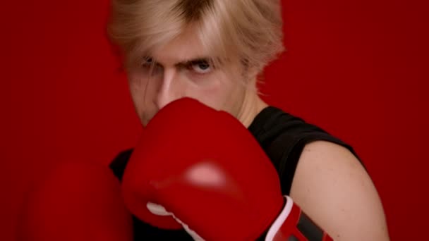 Боксерський удар. Молодий професійний боєць в боксерських рукавичках робить удар вперед на камеру, червоний фон — стокове відео