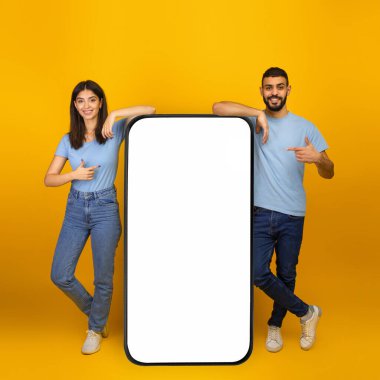 Harika bir mobil uygulama. Genç Arap çift boş ekran modeliyle akıllı telefonu işaret ediyor, uygulamayı veya web sitesini tanıtıyorlar