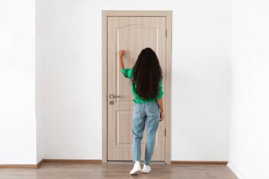 Arkadan bakan kadın ahşap kapıyı çalıyor.